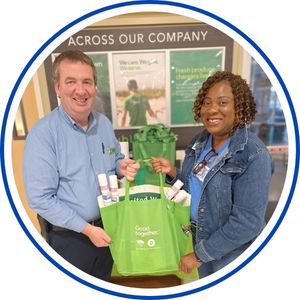 A United Way North Central Florida staff member presents a green reusable grocery tote filled with items to a Publix employee in appreciation for their partnership.