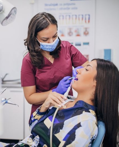 A dental hygienist leans over a patient gently cleaning their teeth.